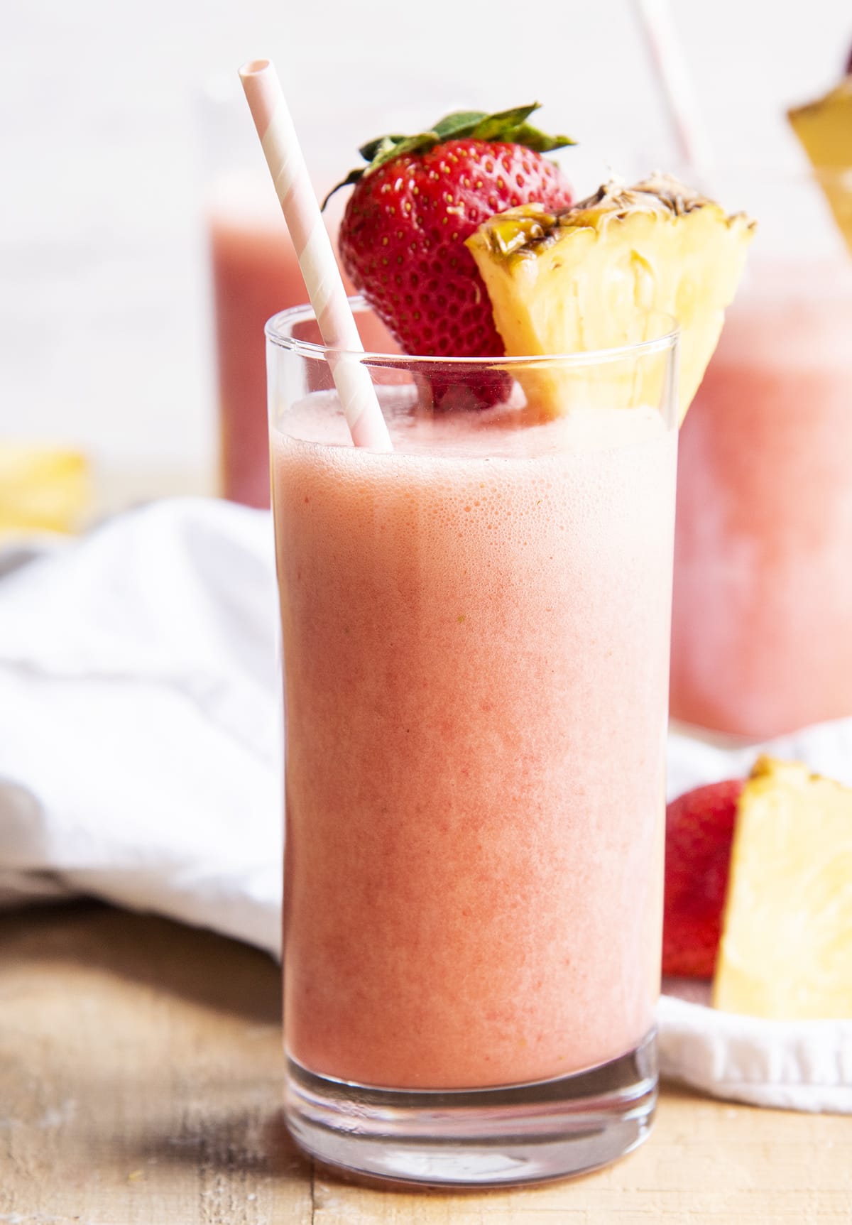 A glass of a pink strawberry blonde drink topped with a pineapple wedge, and a strawberry.