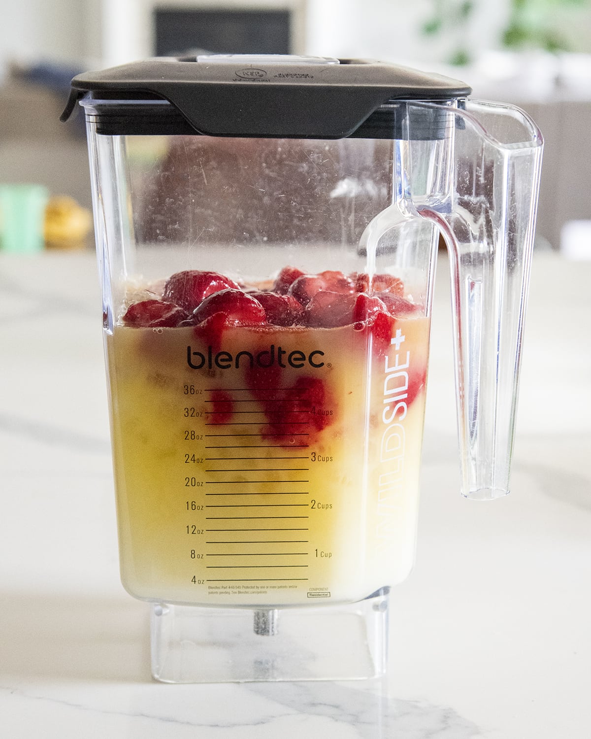 A blender full of a yellow liquid and strawberries.