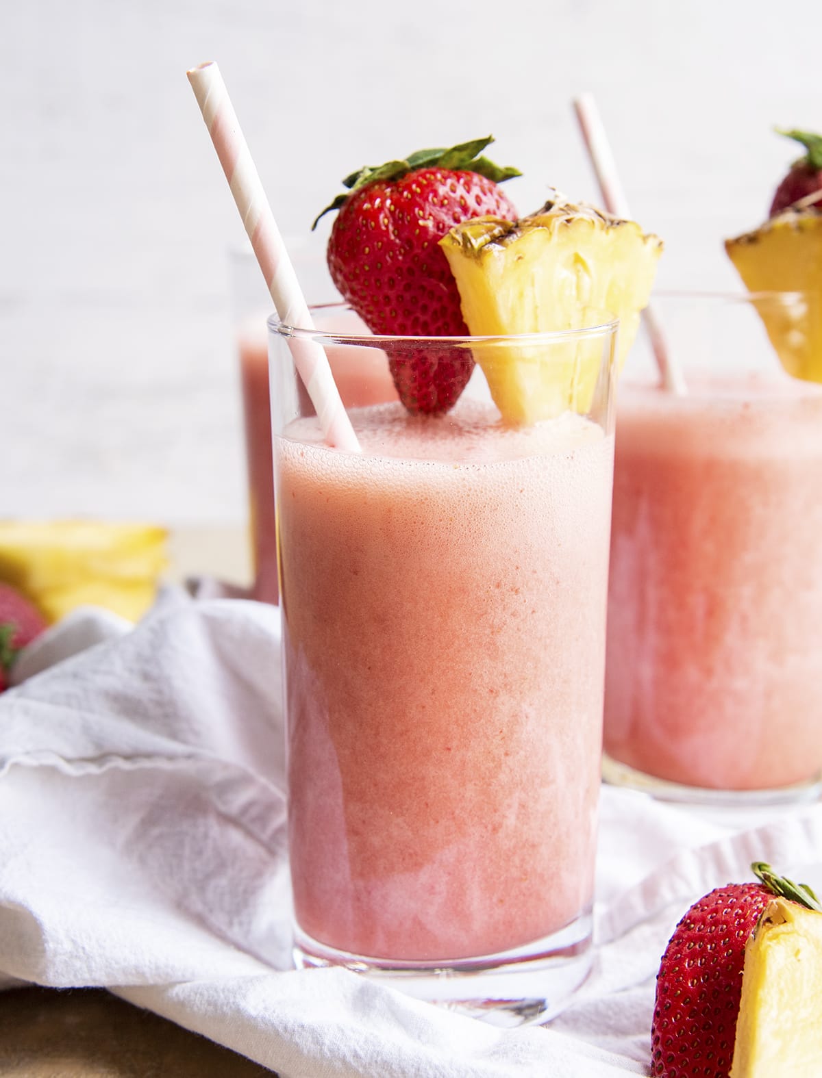 Glasses of a strawberry pina colada drink topped with a strawberry and pineapple piece.