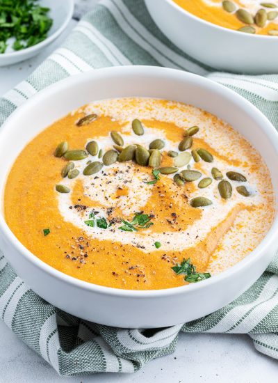 A bowl of tomato and squash soup topped with cream, pumpkin seeds, and fresh parsley,
