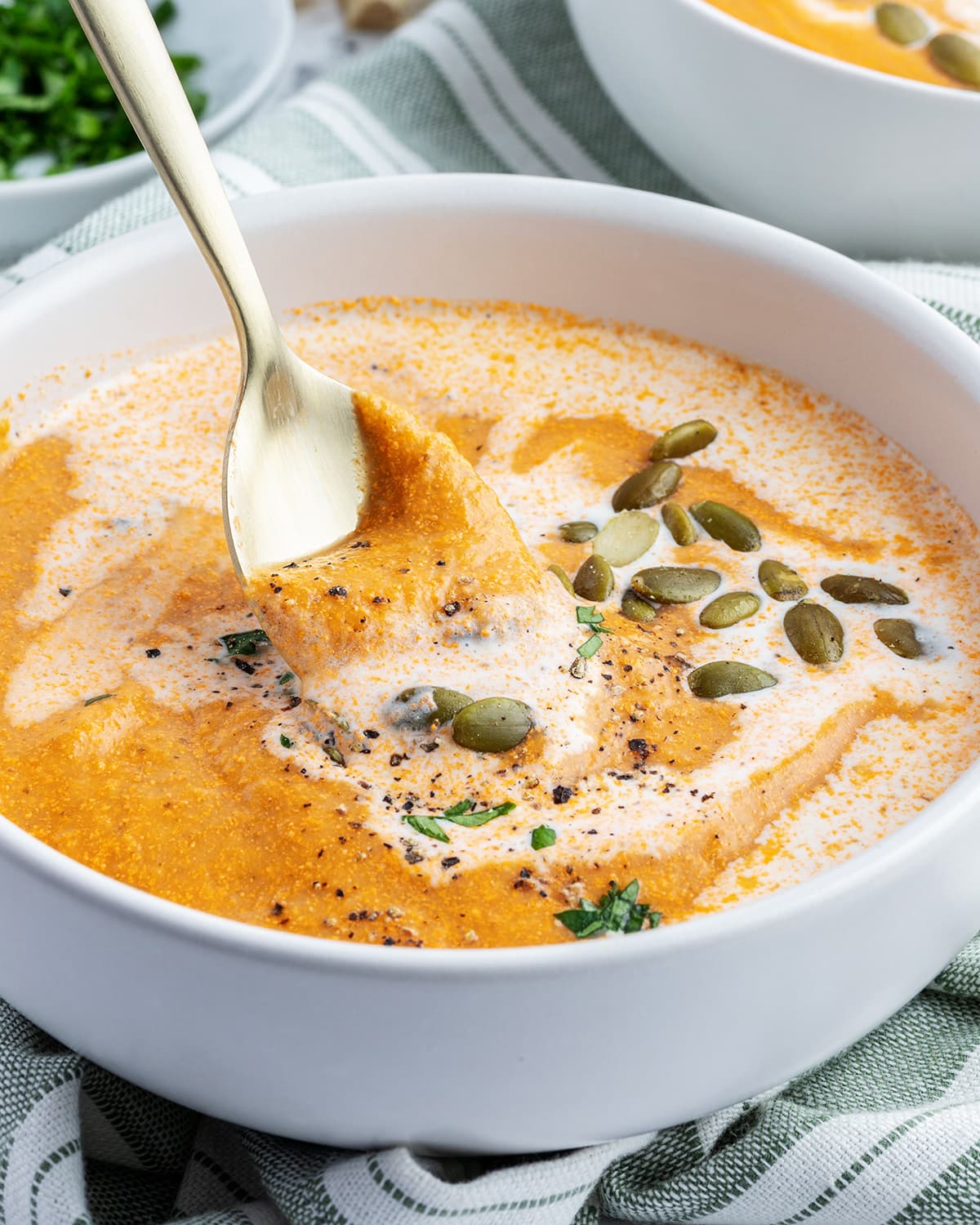 A spoon lifting out of a bowl of tomato and squash bisque.