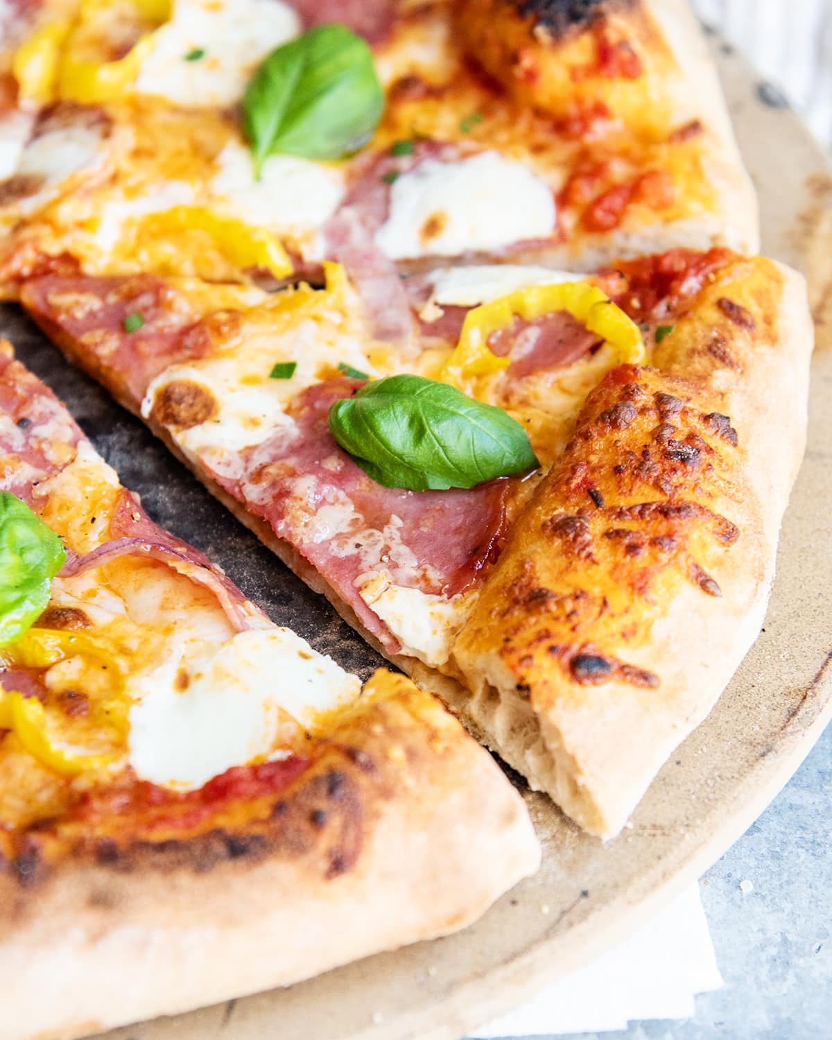 A close up photo of a slice of salami pizza with banana peppers, and a fresh basil leaf on top.