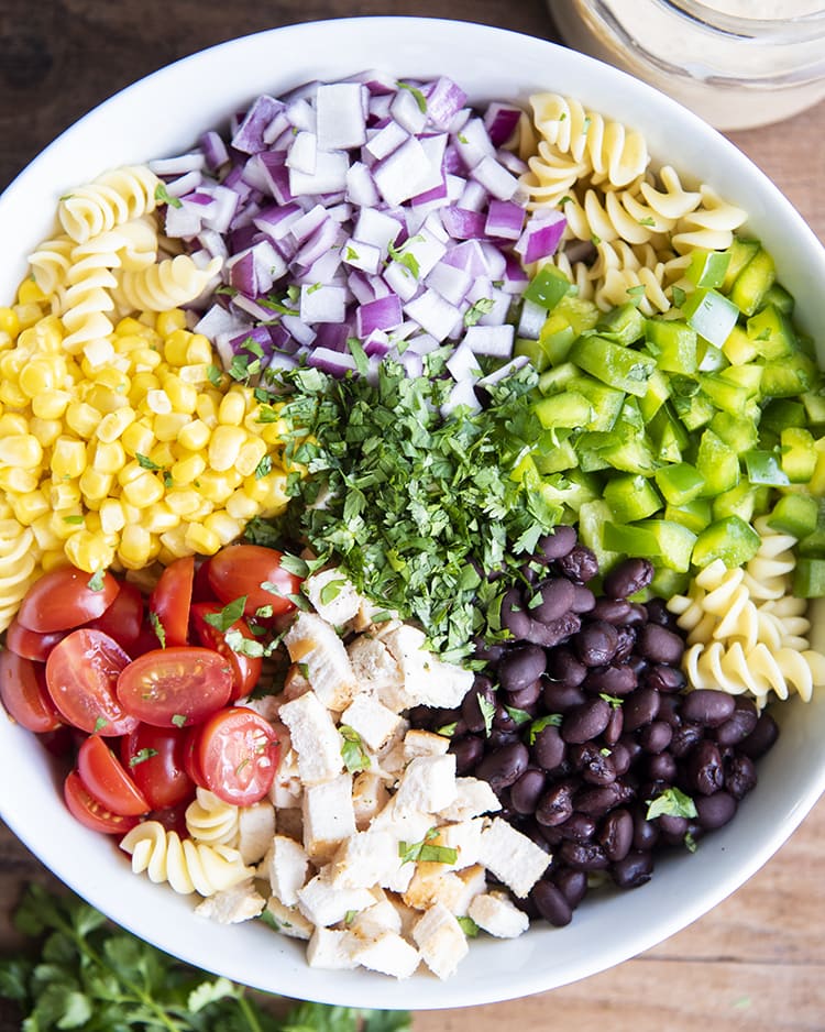 A bowl of noodles, red onion, bell peppers, black beans, chicken, tomatoes, corn, and cilantro