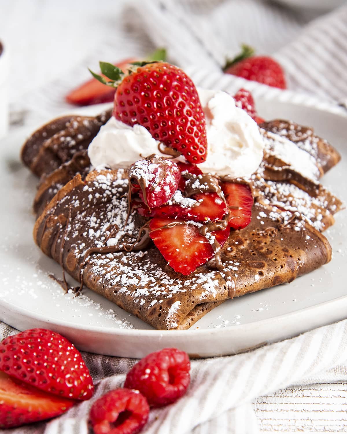 A plate of chocolate crepes folded up into quarters and topped with strawberries and nutella.