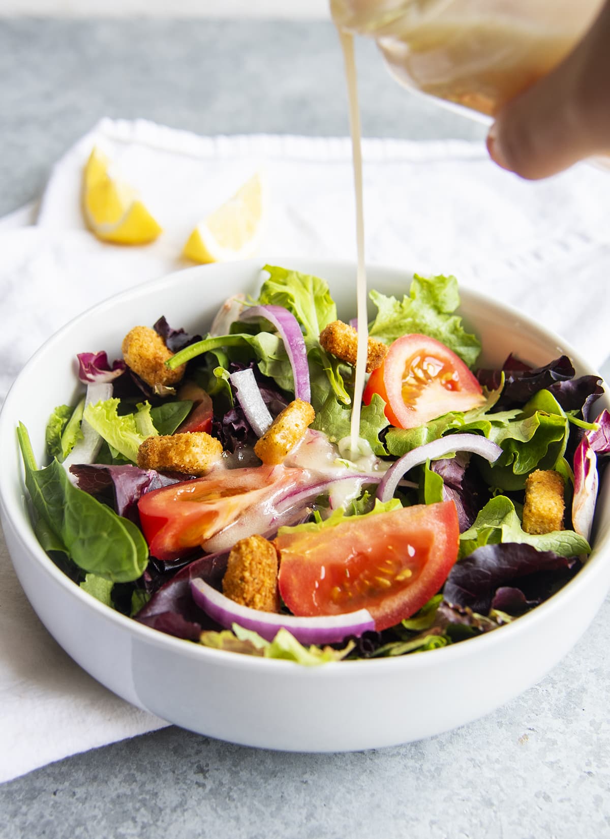 Lemon dijon dressing being poured on a salad in a bowl.
