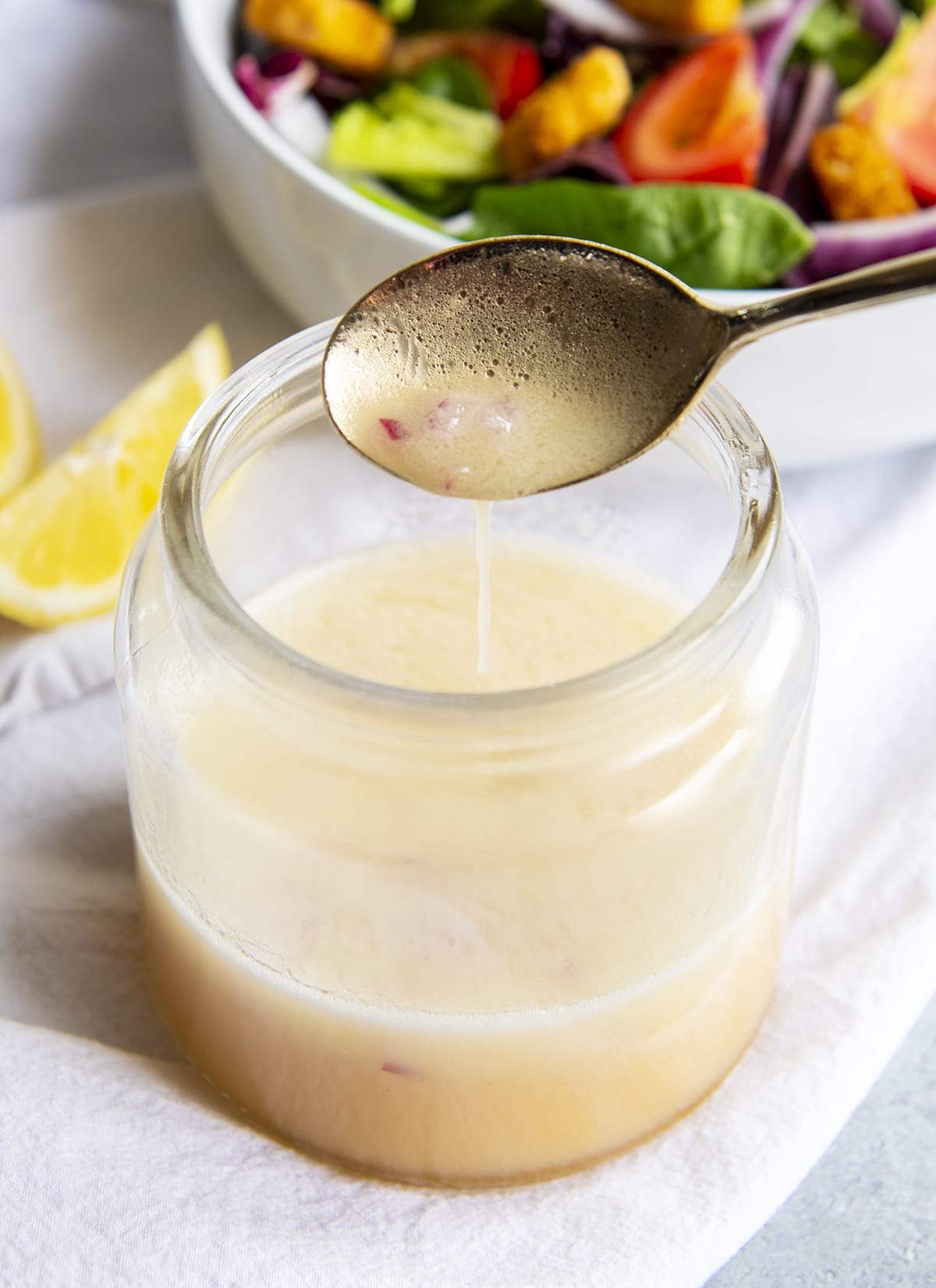 A spoon above a jar of lemon dijon dressing.