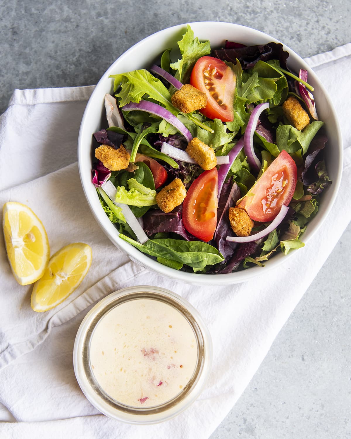 An overhead photo of a bowl of salad and a jar of lemon salad dressing.