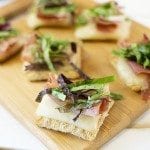 Front view of prosciutto and mixed greens triscuit crackers on a wooden board.