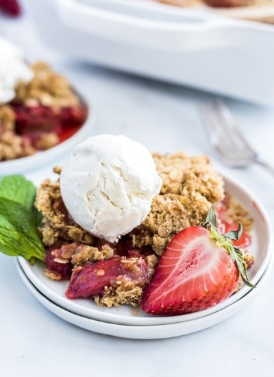 Strawberry Crumble on a white plate with a fresh strawberry and a scoop of vanilla ice cream