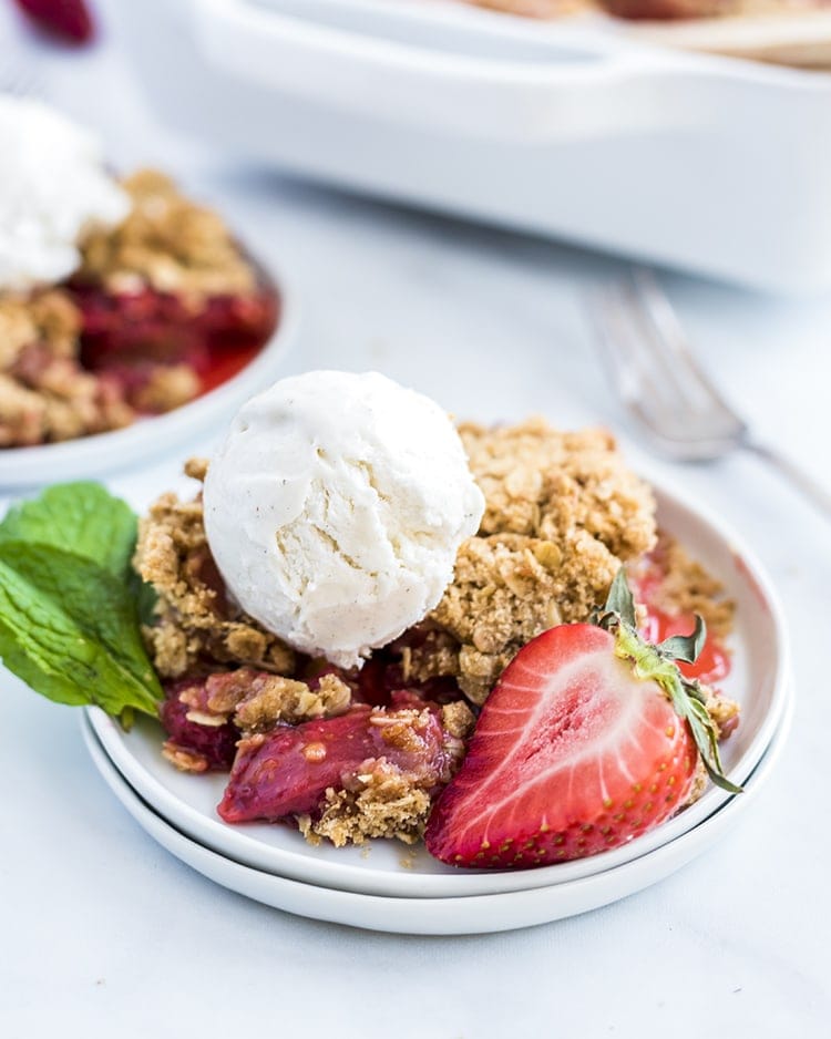 Strawberry Crumble on a white plate with a fresh strawberry and a scoop of vanilla ice cream