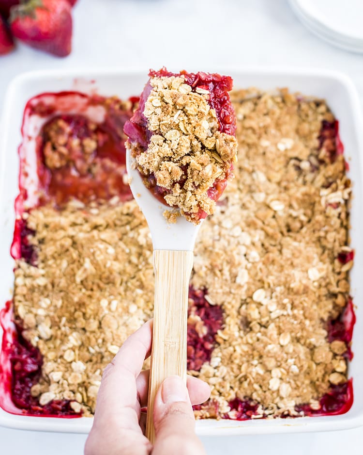 A scoop of strawberry crumble with a pan of it below.