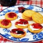Angled view of cherry berry jelly on top of crackers on a white and blue plate.