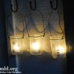 Three hanging decorated mason jars with lights inside.