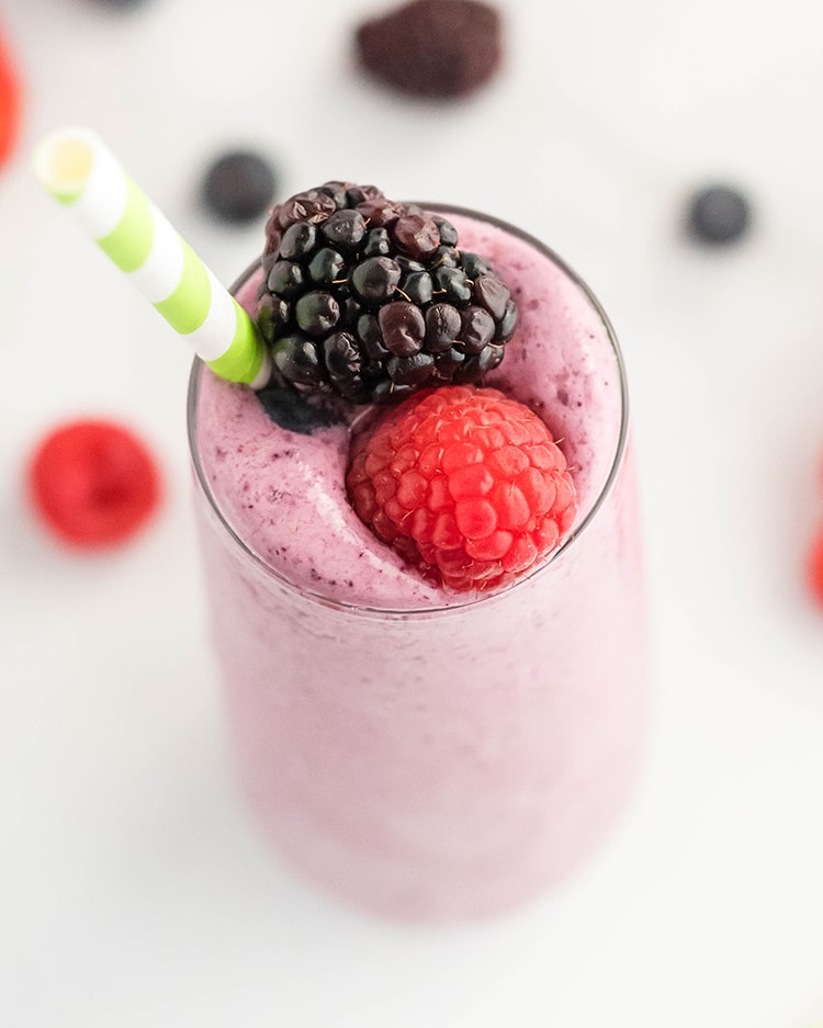 Close up image of a glass filled with mixed berry julius topped with berries and a straw.