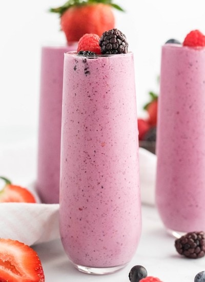 Close up image of three glasses filled with mixed berry julius topped with berries.