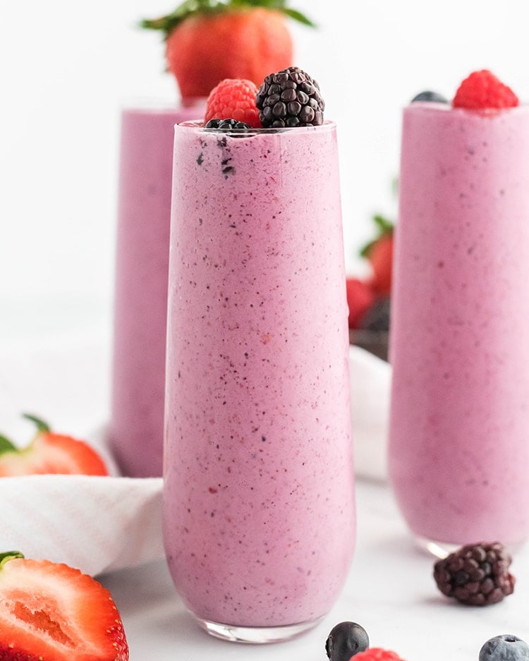 Close up image of three glasses filled with mixed berry julius topped with berries.