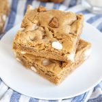 A square image of two cookie bars stacked with biscoff cookies and white chocolate chips in them.