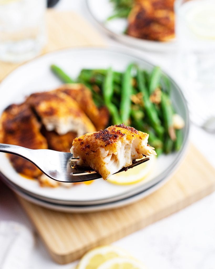 A bite of blackened tilapia on a fork above the plate of the dish.