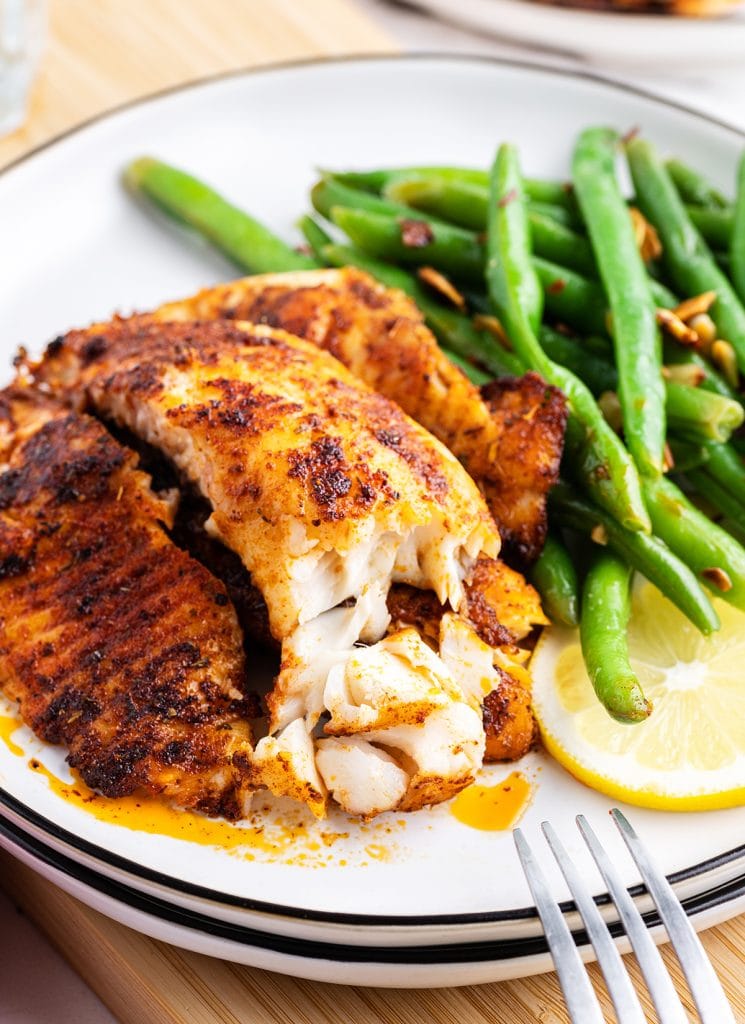 A piece of blackened tilapia with a black reddish crust, with a bite taken out of the front to show the flaky white meat.