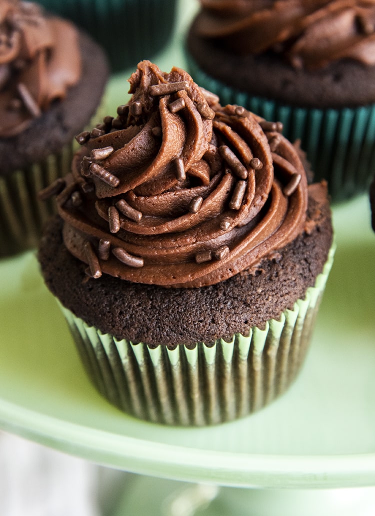 A close up of a chocolate cupcake on a green cake stand.