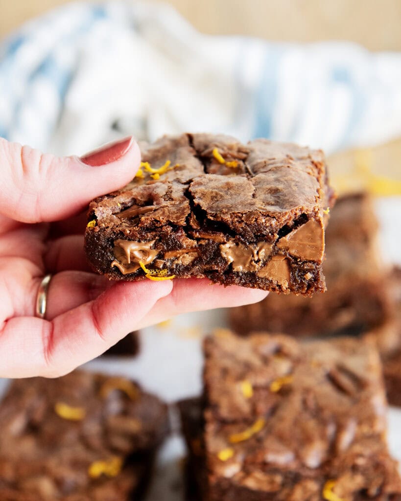 A hand holding a chocolate orange brownie full of melted chocolate orange candies.