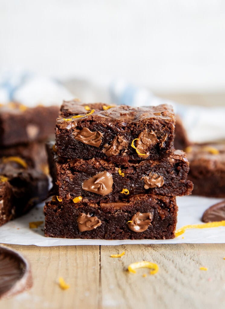 A stack of 3 chocolate brownies, with melty pieces of chocolate in them, and orange zest pieces.