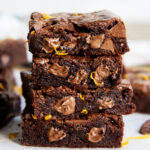 A stack of 4 chocolate brownies, with melty pieces of chocolate in them, and orange zest pieces.