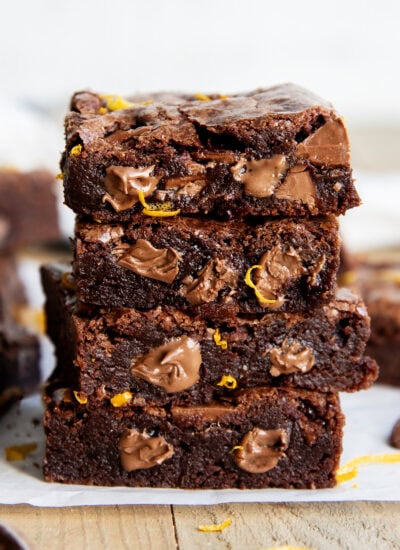 A stack of 4 chocolate brownies, with melty pieces of chocolate in them, and orange zest pieces.