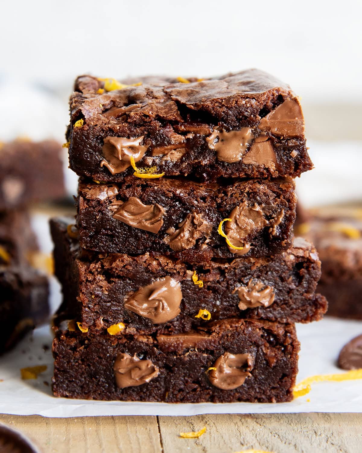 A stack of 4 chocolate brownies, with melty pieces of chocolate in them, and orange zest pieces.