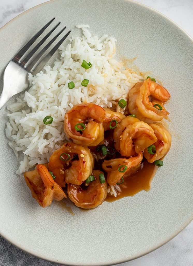 A small grey plate half full of honey glazed shrimp, and the other half full of white rice. They are both sprinkled with sliced green onions.