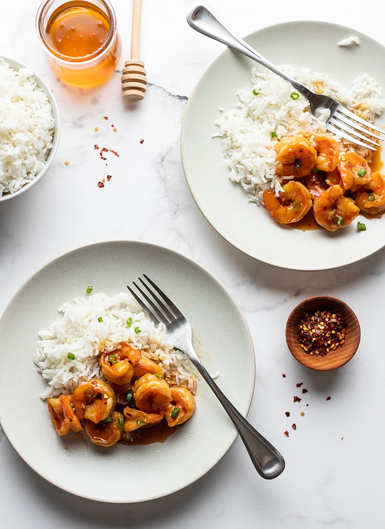 Two small plated of a shrimp and rice. The shrimp has an orange colored glaze on it.
