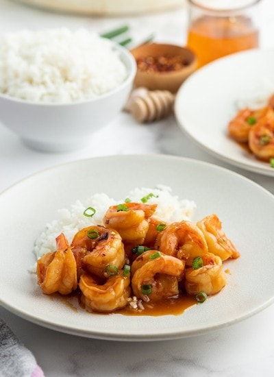 A plate of shrimp with an orange reddish sauce on it, and sprinkled with green onions.