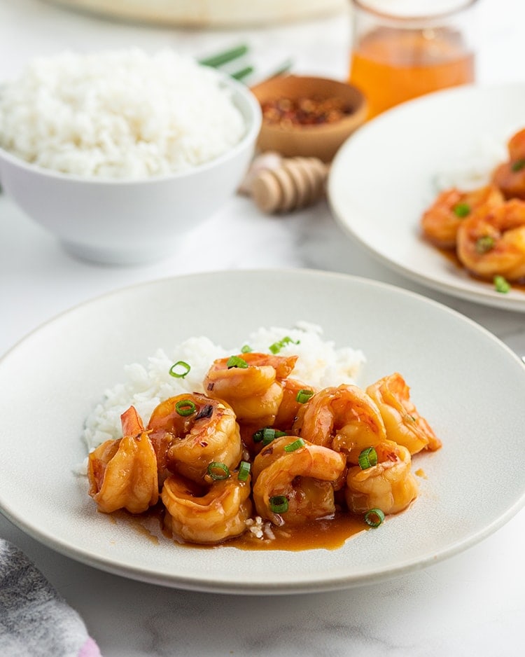 A plate of shrimp with an orange reddish sauce on it, and sprinkled with green onions.