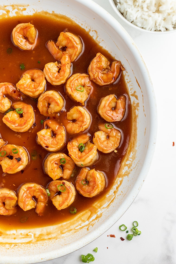 Shrimp cooking in a reddish sauce in a saute pan. Sprinkled with green onions.