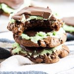 A stack of three mint brownie cookies, the top cookie has a bite taken out of it.