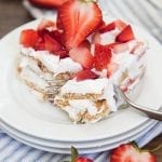 A piece of strawberry ice box cake on a plate topped with fresh strawberries.