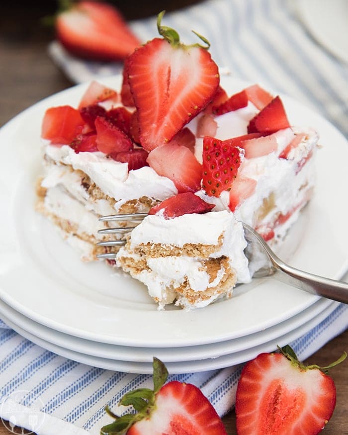 A piece of strawberry ice box cake on a plate topped with fresh strawberries.