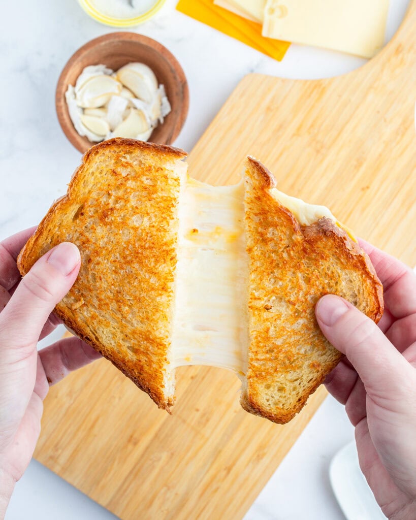 A hand pulling two halves of a grilled cheese sandwich apart, showing the gooey cheese in the middle.