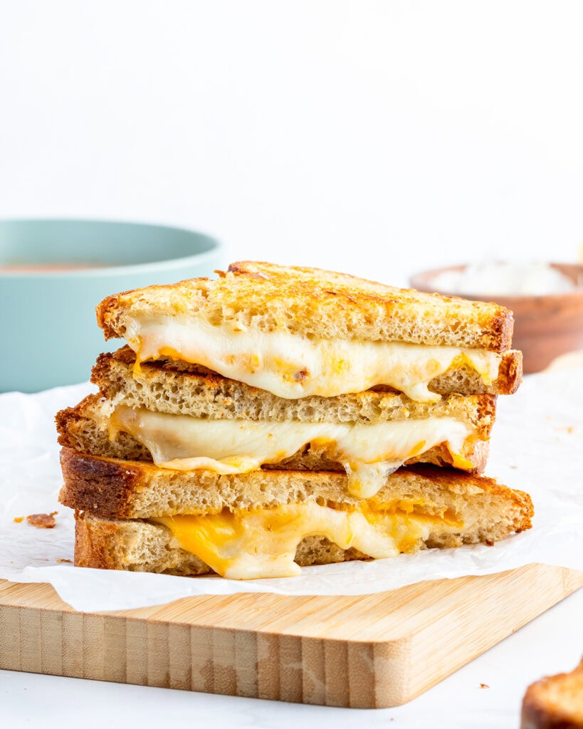 A stack of halves of a grilled cheese sandwich showing the gooey cheese coming out the middle.