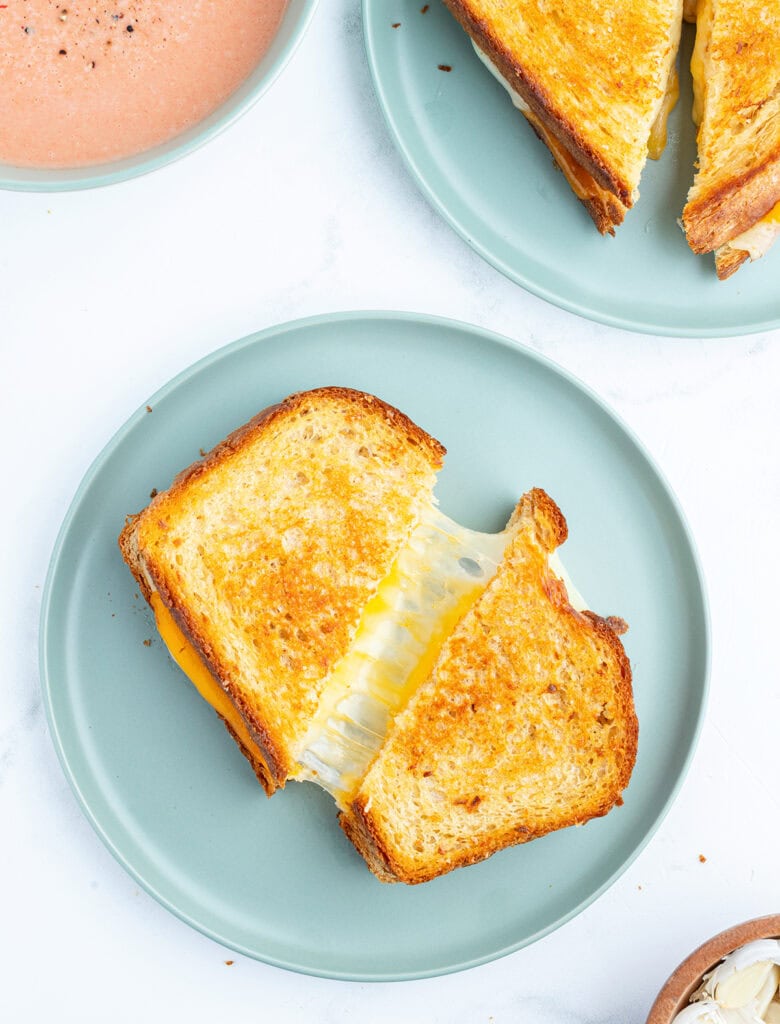 A garlic butter grilled cheese sandwich on a plate with gooey cheese between the two halves of the sandwich. 