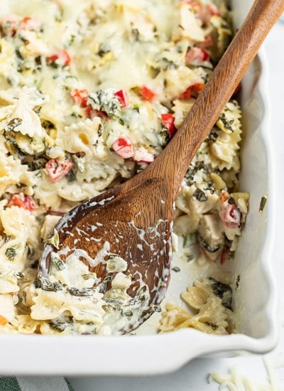 Close up image of spinach dip pasta being scooped with wooden spoon in white dish.