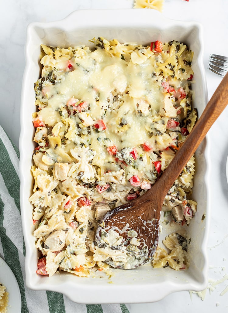 Close up image of spinach dip pasta being scooped with wooden spoon.