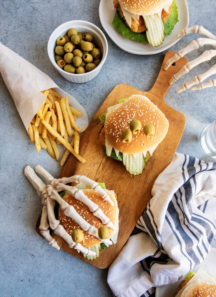 An above view of chicken sandwiches on a wooden board, they are decorated to look like monsters. 
