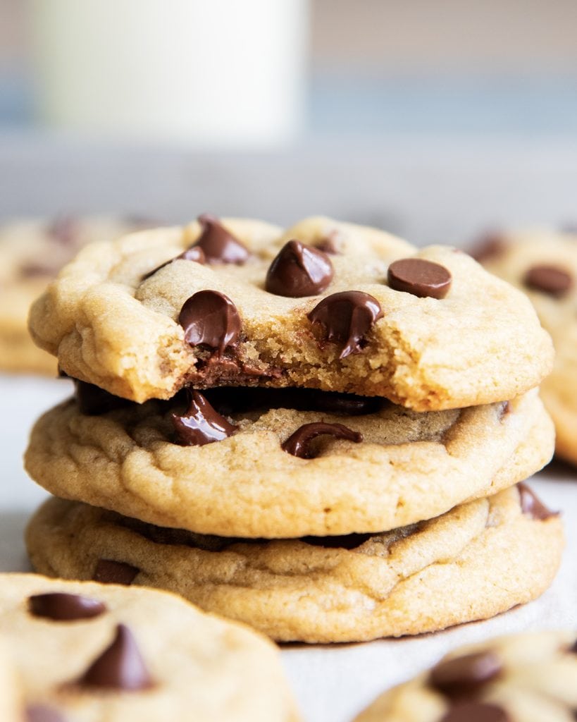 A stack of three chocolate chip cookies, and the top cookie has a bite out of it.