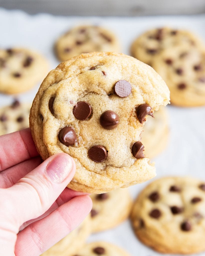 A hand holding a chocolate chip cookie with a bite out of it.