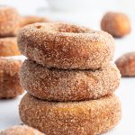A stack of three cinnamon sugar donuts with more donuts behind them.
