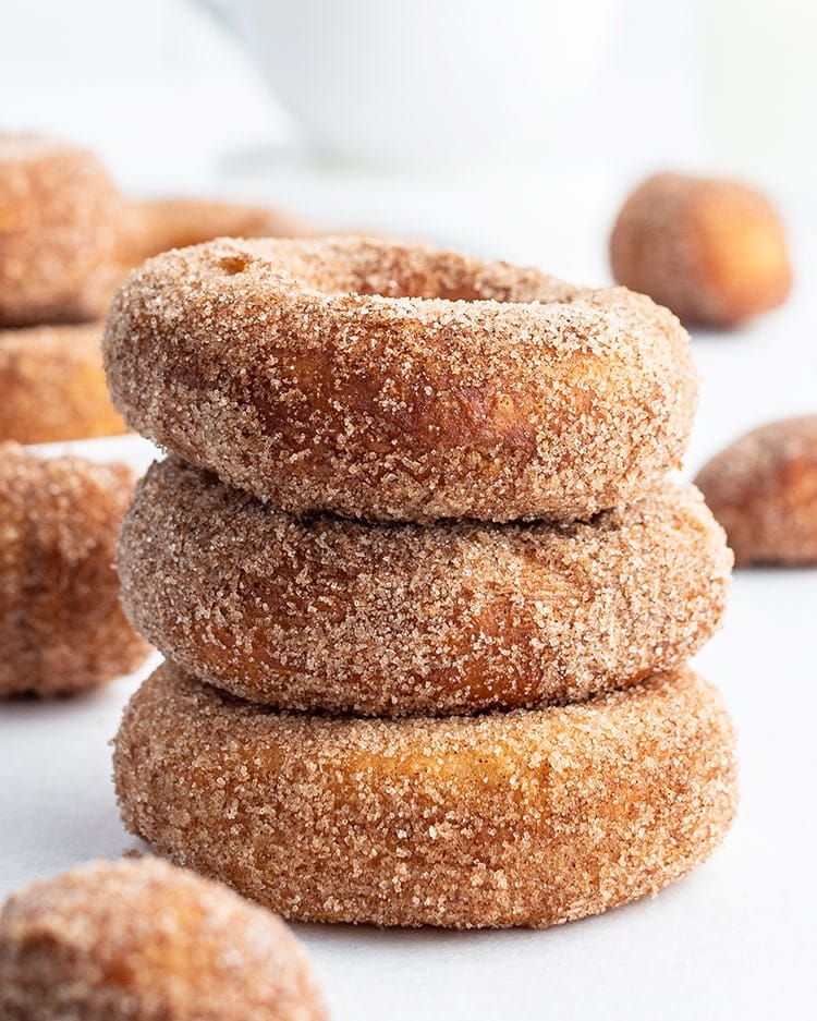 A stack of three cinnamon sugar donuts with more donuts behind them.