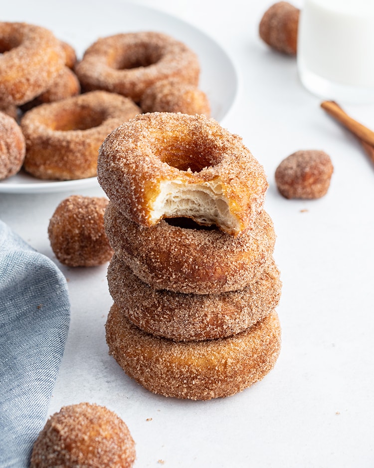 A stack of cinnamon sugar biscuit donuts, and the top donut has a bite out of it showing the middle.