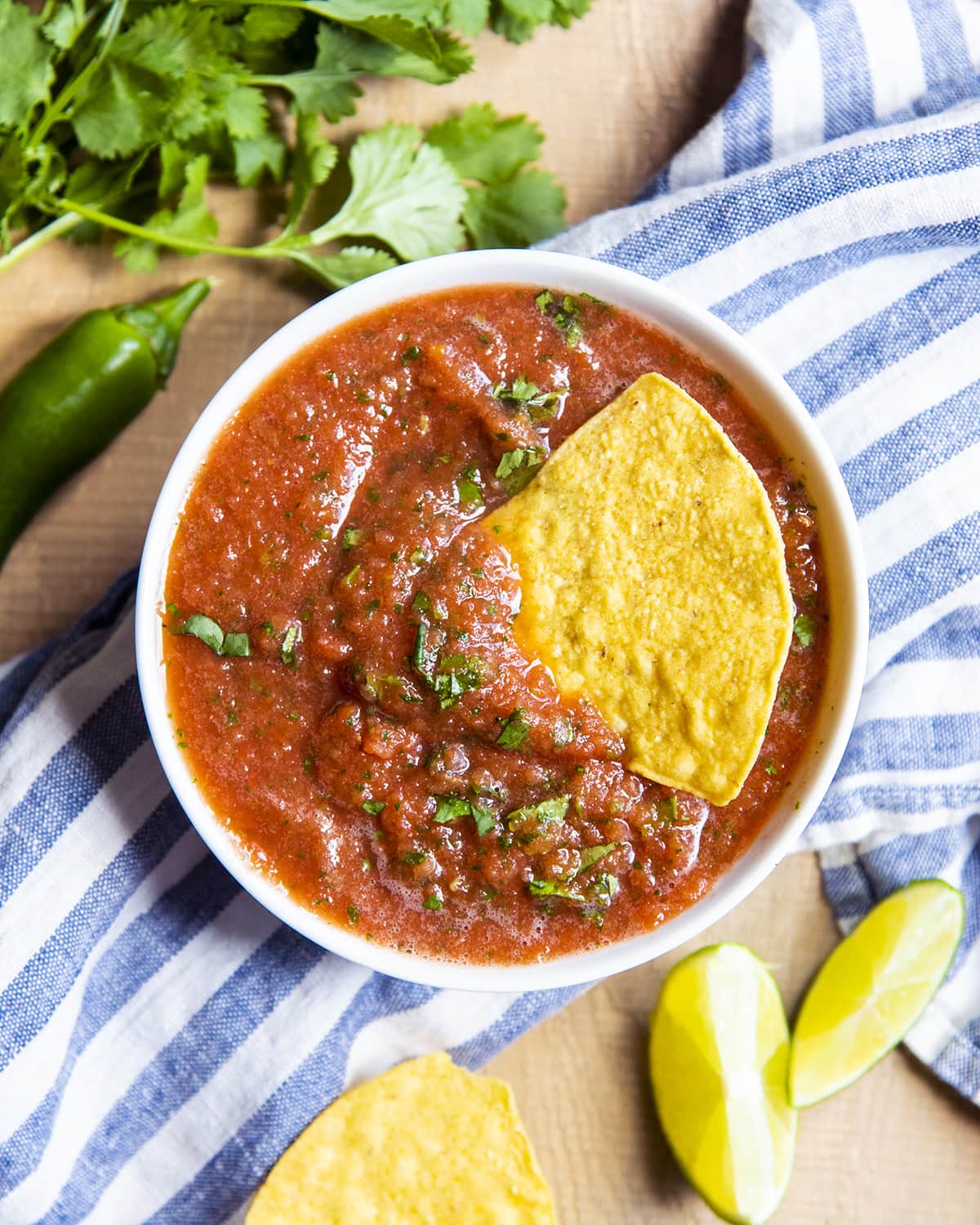 An overhead shot of a bowl of restaurant style salsa with a chip in the bowl.
