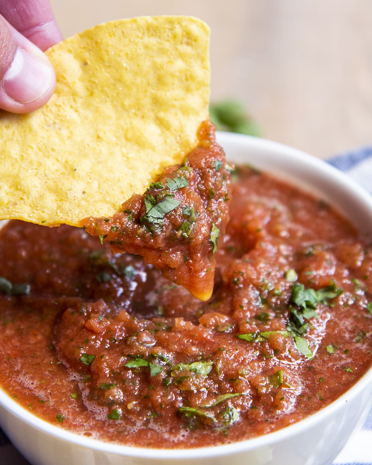 A close up of a hand dipping into a bowl of salsa with a chip.